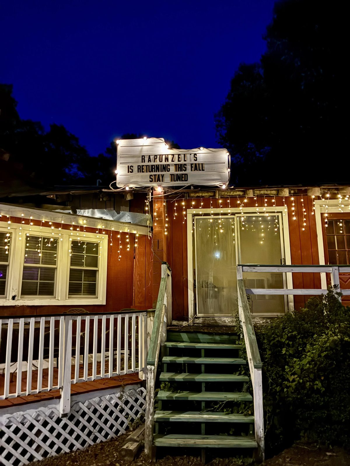 The front steps at dusk: green stairs up to the barn-red building, icicle lights along the eaves, the lit letterboard above.